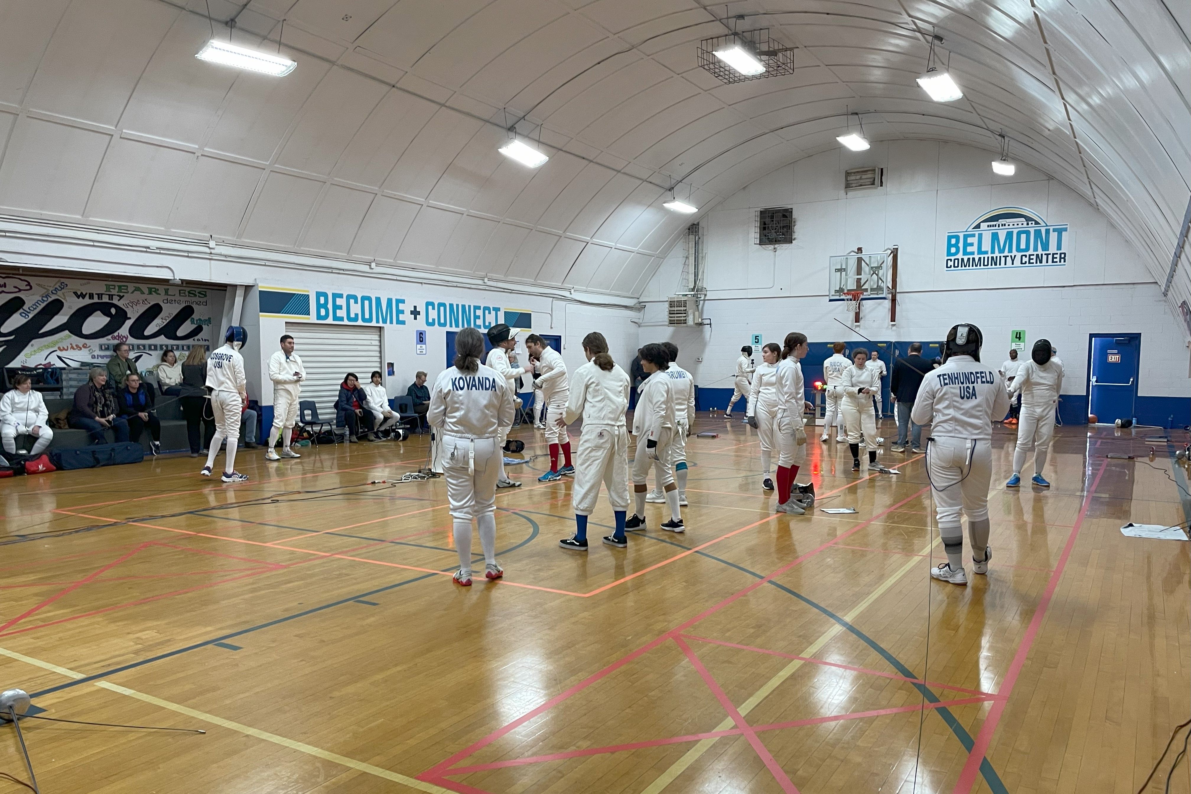 Gym with arched ceiling and hardwood floors filled with epee fencers